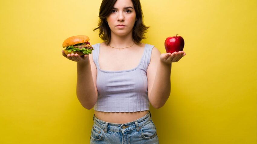 Dziewczyna dokonuje wyboru między zjedzeniem jabłka a hamburgera.